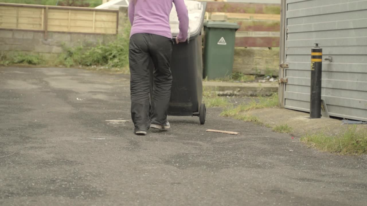 Woman wheeling out grey garbage bin
