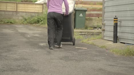 woman wheeling out grey garbage bin