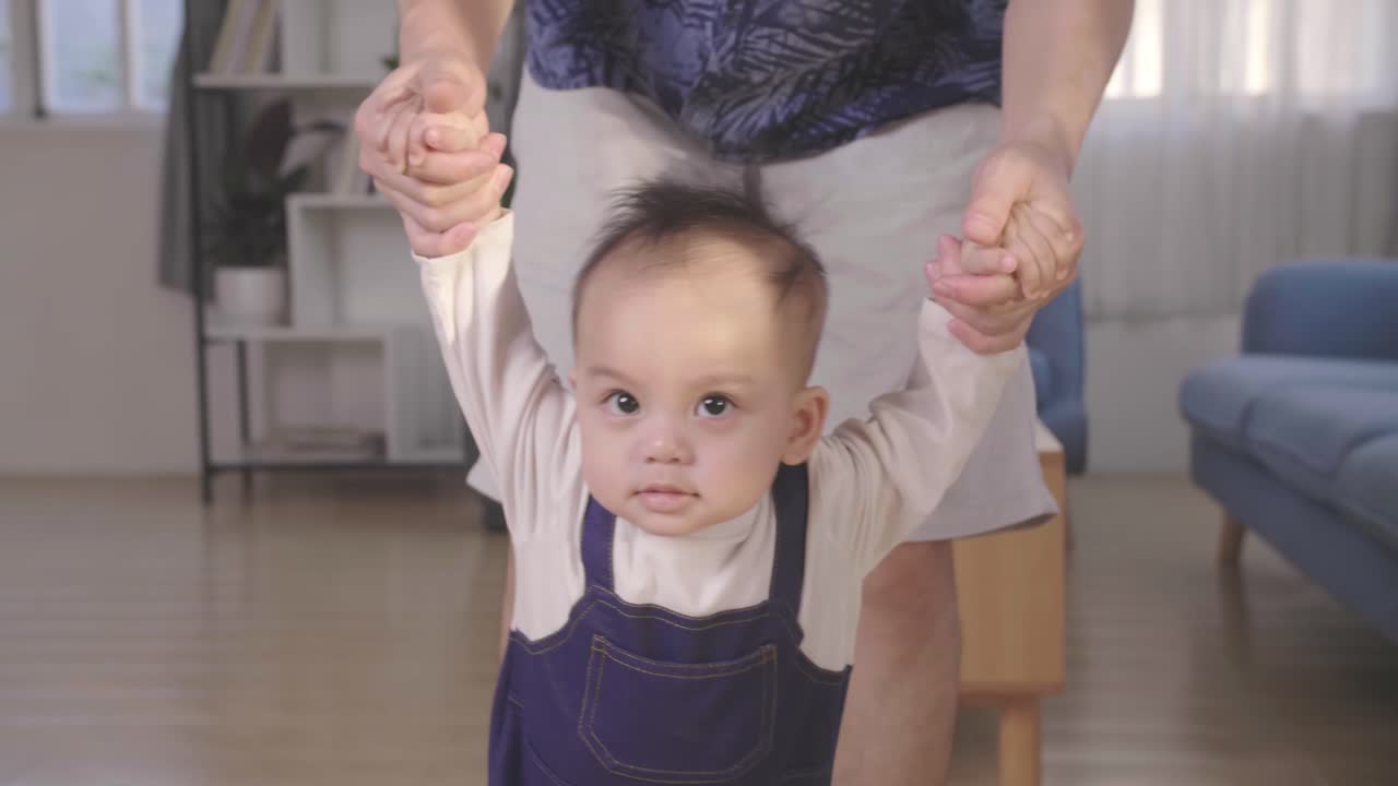 Baby Boy Learning To Walk And Make His First Steps. Father Is Holding His Hand