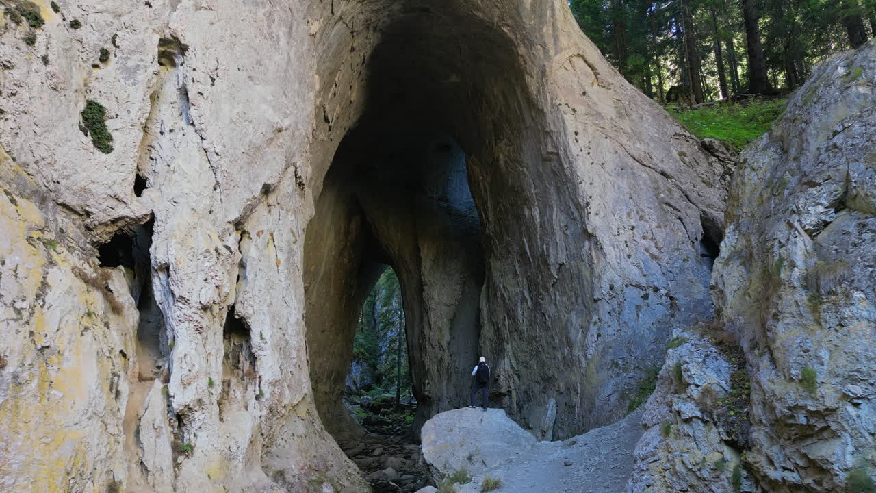 WONDERFUL BRIDGES: Lone hiker standing near towering rock arch framed by lush mountain forest, showcasing dramatic geological landscape with natural stone formation. Bulgaria