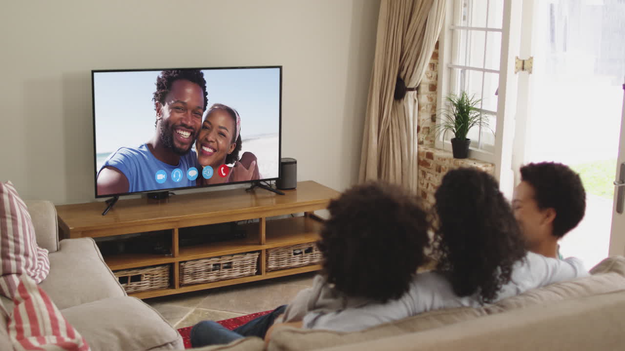 Famiglia afroamericana seduta sul divano che fa una videochiamata con amici sullo schermo della TV.