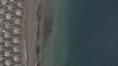 flat lighting aerial descends toward beach umbrellas on sand beach