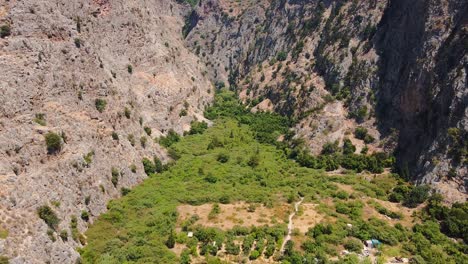 Aerial-top-down-dolly-shot-in-valley-with-green-trees-and-some-houses-between-rock-formations