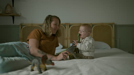 mother and baby playing with dinosaurs on a bed