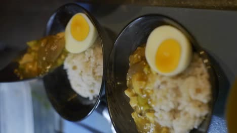 curry de tofu cremoso en cuchara en un cuenco negro con huevo y arroz, filmado como una toma vertical en cámara lenta al estilo deslizante