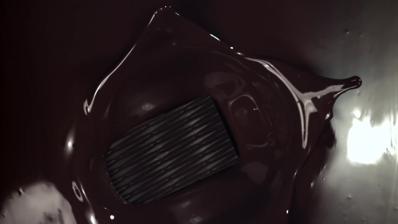 Tavoletta di cioccolato fondente sommersa in ricco cioccolato fuso al rallentatore.