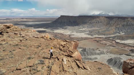 Toma-De-Drone-De-Una-Mujer-Caminando-Sola-En-La-Cima-De-Una-Mesa-Sobre-Un-Profundo-Cañón,-Un-Abismo-Y-Un-Paisaje-Desértico.