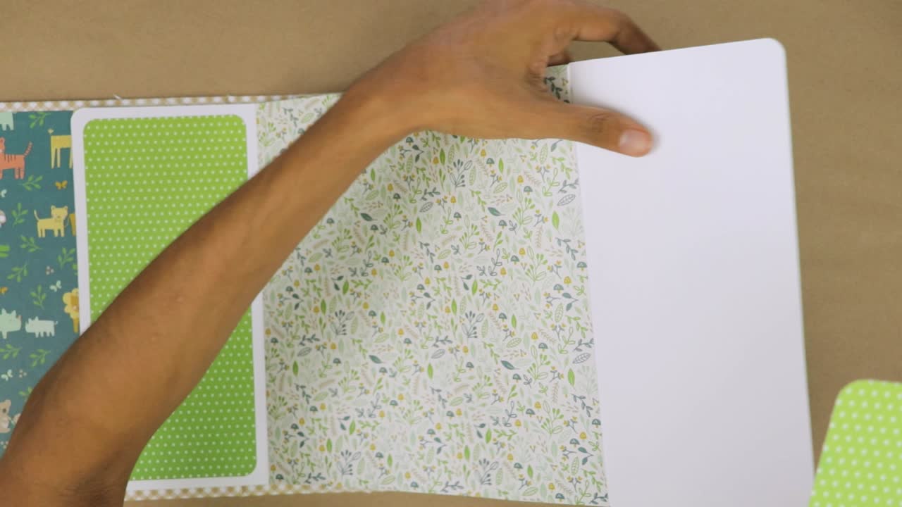Crafting colorful baby scrapbook album with glue and patterned papers, top-down view, close-up