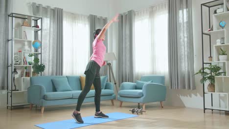 una hermosa chica asiática en forma con un traje atlético rosa está haciendo ejercicio enérgicamente en su sala de estar