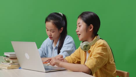 close up of asian woman student teaching her friend on a laptop while sitting on a table in the green screen background classroom