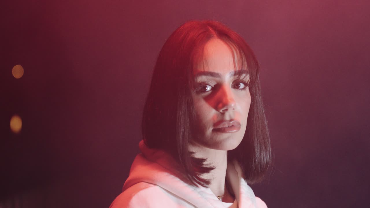 Young beautiful woman with white sweater. in the night looking into the camera, dark environment and fog, red light