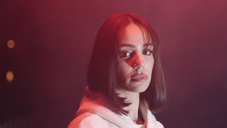 young beautiful woman with white sweater. in the night looking into the camera, dark environment and fog, red light
