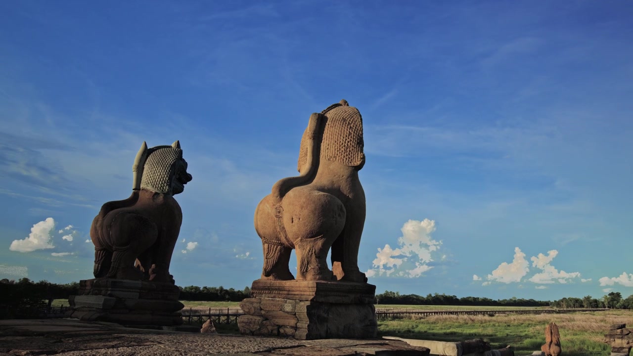 Yağmur mevsiminin başlangıcında otlarla dolu baray gölüne bakan bir çift Angkor dönemi kumtaşı aslan heykeli. Hareketli bulutlar ve mavi gökyüzü için boş alan ile hareket kontrollü dinamik hareket hızlandırılmış çekim.