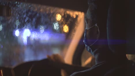 the young man in medical mask is sitting in the car on the rainy evening