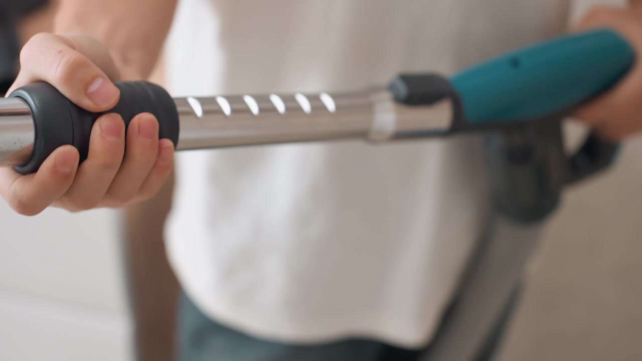 Hands adjusting telescopic vacuum wand near kitchen counter, operator tightening metal tube connector, turquoise handle click lock, ergonomic grip preparing appliance for floor cleaning, routine