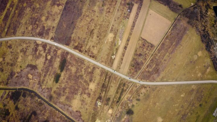 Aerial view high above car driving through dry farm land road trip flying over car on empty country road in barren landscape 4k footage of cars on road