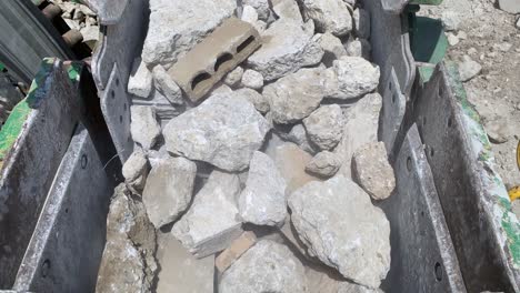 rocks and concrete being fed into the jaws of a big rock crusher