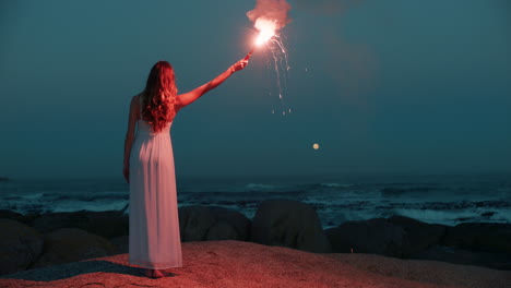 woman lighting signal flare on beach at dawn burning early morning signal