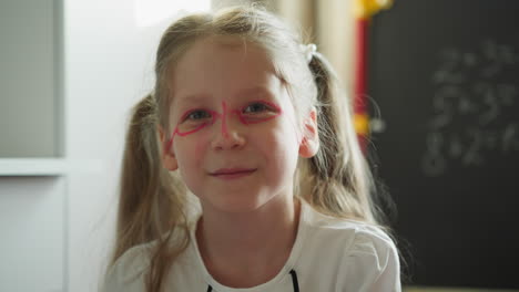 schoolgirl with painted face smiles sitting near blackboard