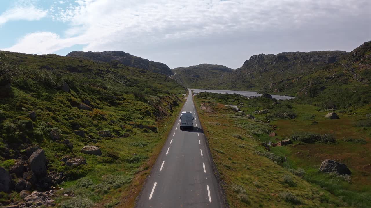 Long, empty road in Norway with mountains, sky, and a camper van driving