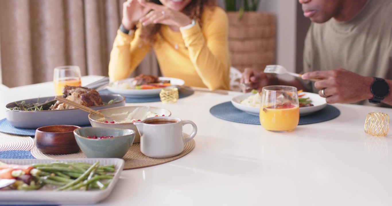 Un couple assis à table, l'homme commence à manger avec une fourchette, la femme gesticule en partageant le repas.