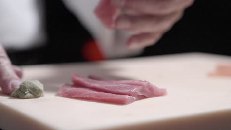 a static shot of a sushi chef placing wasabi on slices of tuna in preparation for sushi. ideal for showcasing sushi-making techniques, ingredient preparation, and japanese culinary skills.