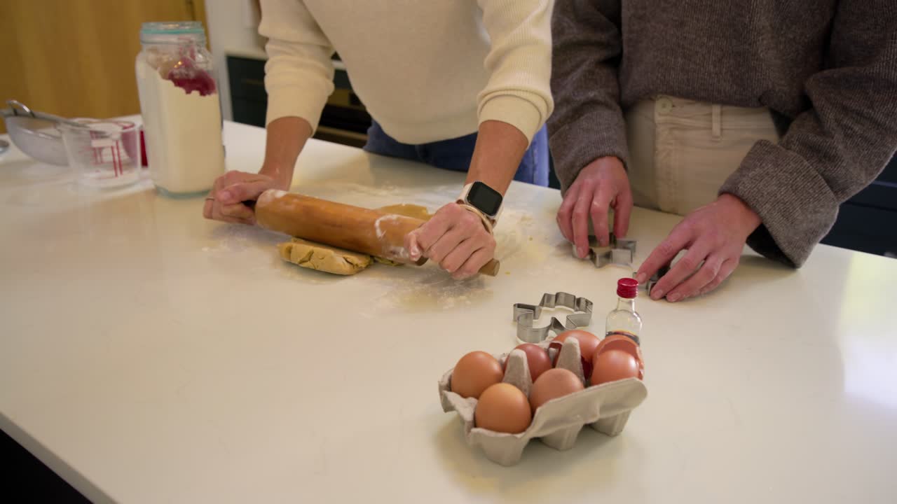 Mother and daughter at counter pressing and rolling dough with pin aligning cutter forming shapes