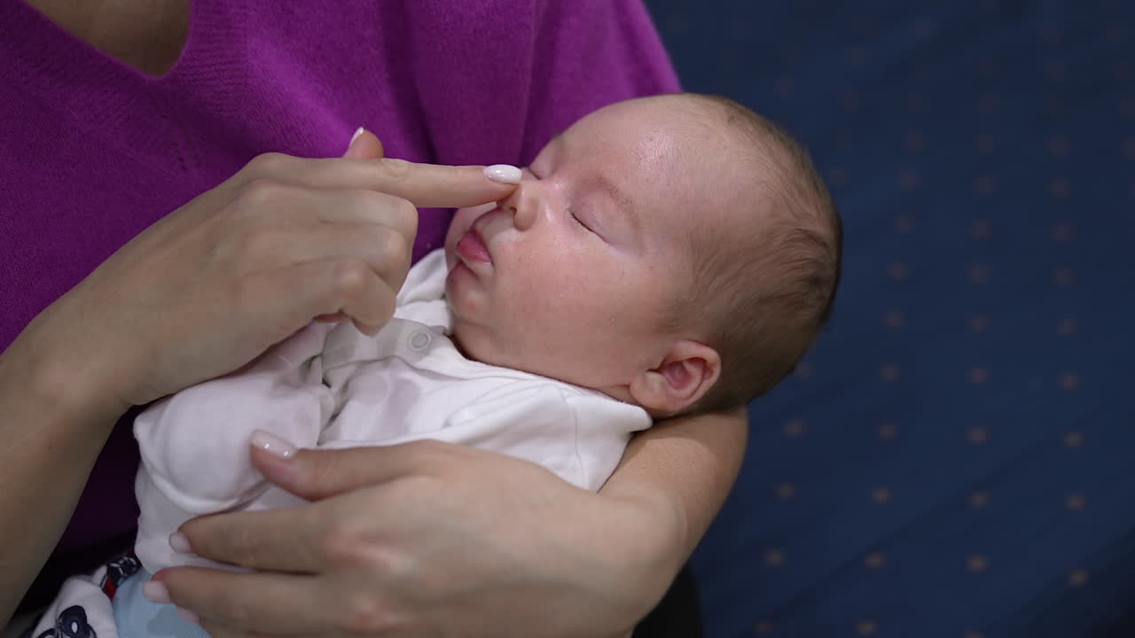 Sweet child sleeping sweetly in mommy's hands. Loving mother trying to wake up her baby but the kid doesn't want to wake up. Close up.