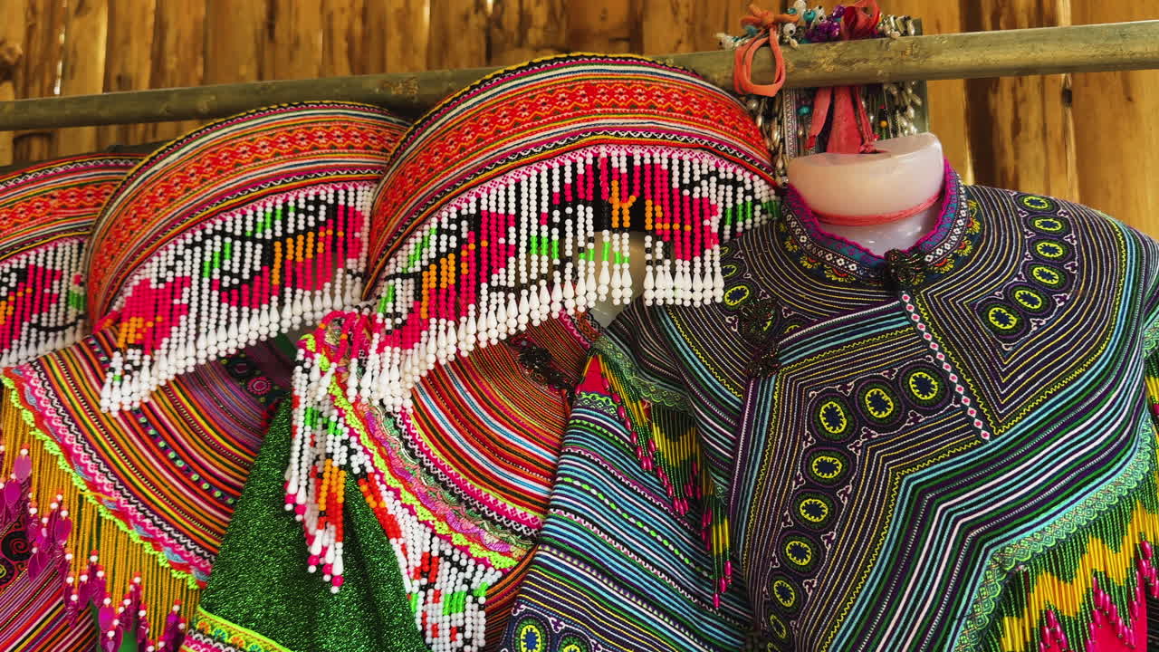 Coloridas prendas tradicionales de tribus de las montañas con tocados de cuentas que cuelgan dentro de una casa de familia de Bac Ha, donde se exhiben bordados complejos, abalorios y patrones ricamente tejidos