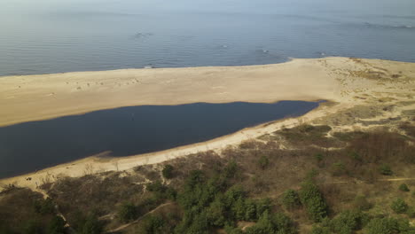 Toma-Aérea-De-Un-Lago-Natural-Rodeado-De-Bancos-De-Arena-Y-Plantas-Y-Un-Tranquilo-Mar-Báltico-En-El-Fondo