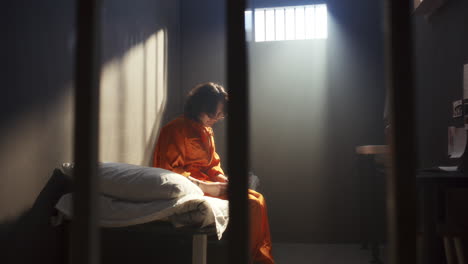 pensive inmate sitting on bed, writing on paper in prison cell