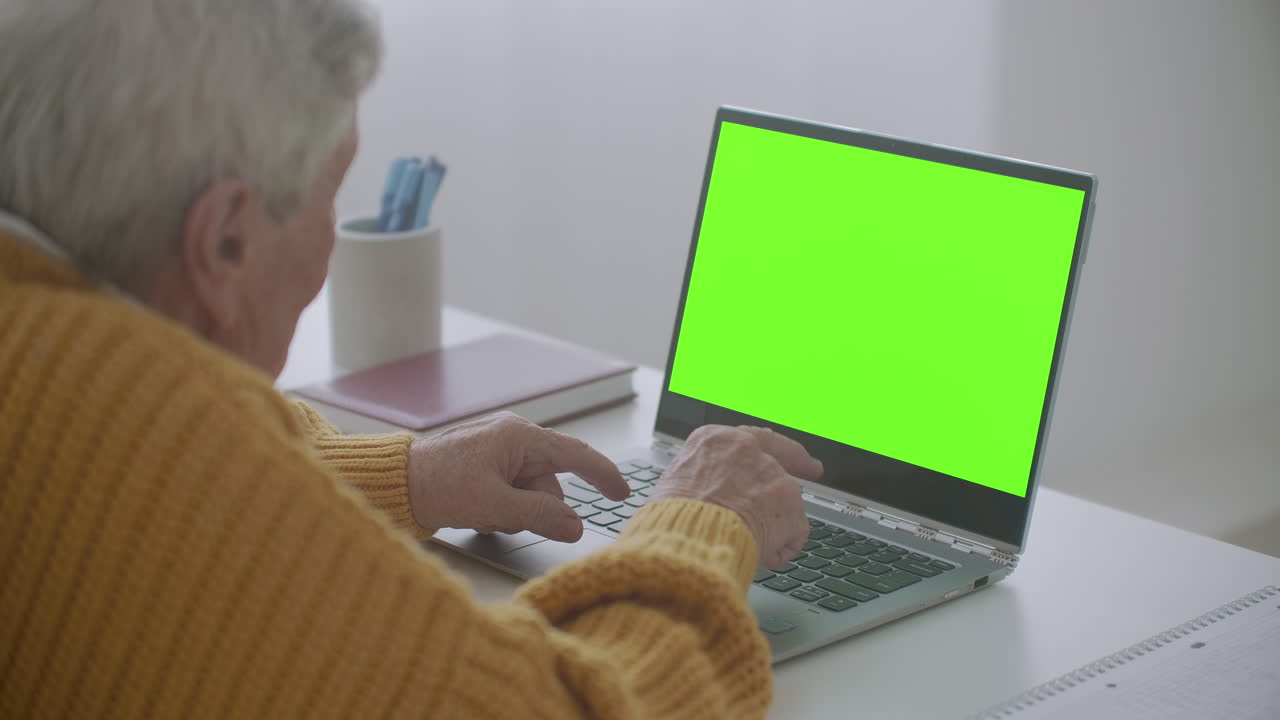 mujer madura asintiendo con la cabeza sí mientras mira una computadora de pantalla verde. mujer madura anciana con cabello gris y una videollamada en su computadora portátil. computadora portátil con pantalla verde