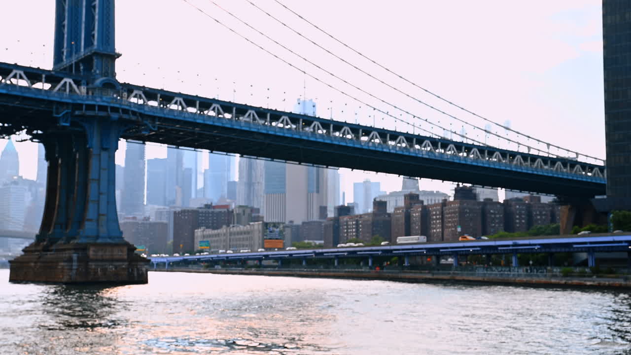 Diverse auto percorrono l'autostrada lungo il lungofiume dell'East River. Visuale dal basso verso il Manhattan Bridge dal paesaggio fluviale
