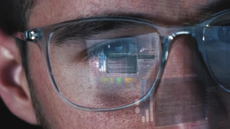 programmer hacker works on computer screen - code is reflected in his eyes and on the glasses - close up