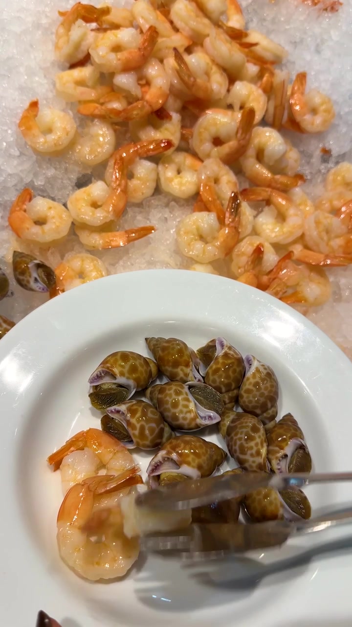 Overhead shot of a person selecting cooked shrimp and sea snails from an ice buffet