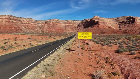 car driving down desert road with bike rack on the back and tall red cliffs in the background. utah state route 261