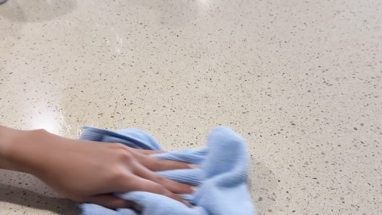A person wipes a coffee spill on a countertop using a cloth, demonstrating effective cleaning