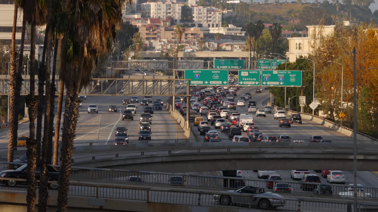 Busy Los Angeles traffic on U.S. Route 101 near Western Avenue and the downtown exit. Palm trees line the road as vehicles move steadily on the freeway, with city buildings in the background