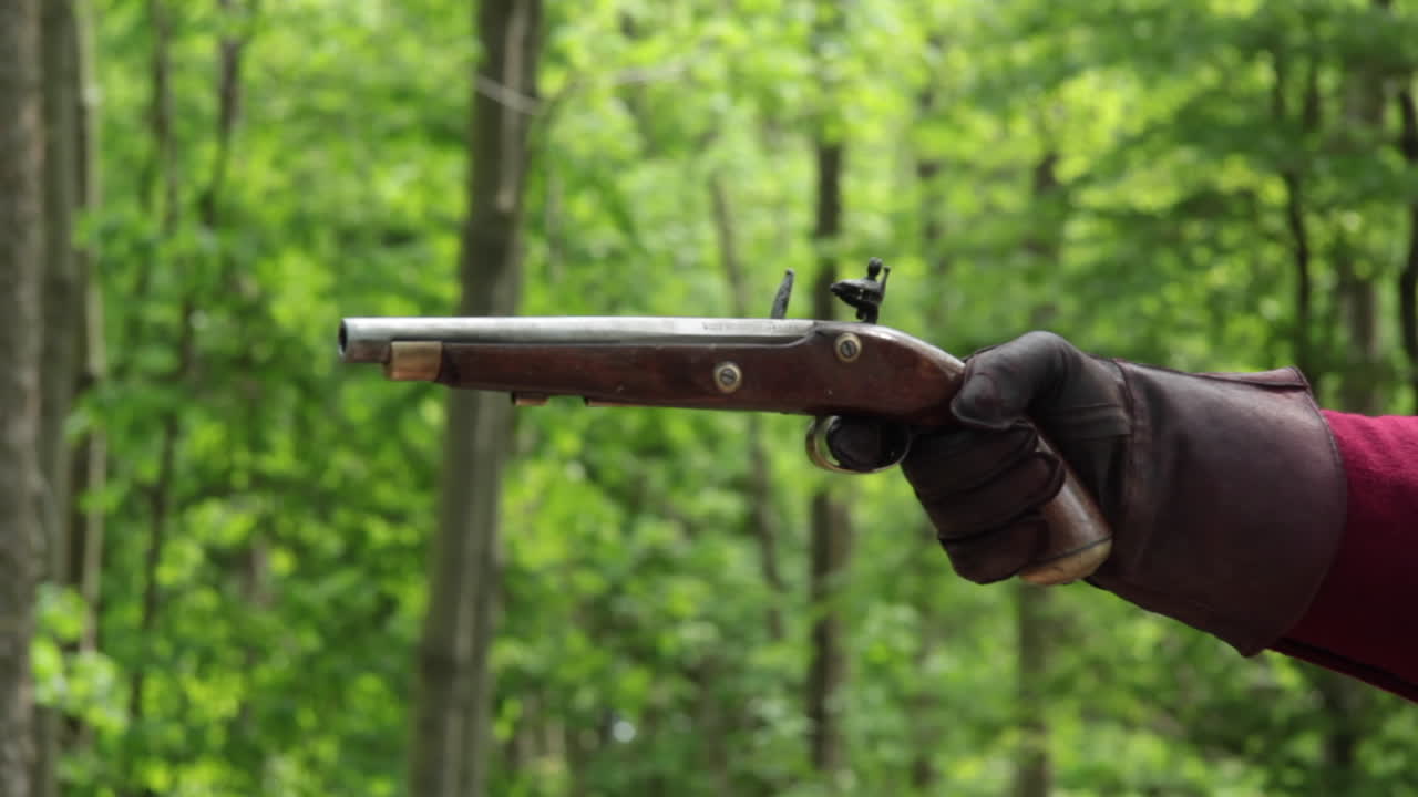 Gloved hand fires antique flintlock pistol in woods, close-up