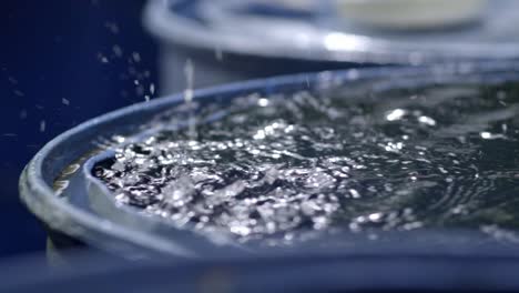 Rain-drops-filling-up-rainwater-harvesting-barrel,-closeup-slow-motion,-slow-zoom-in