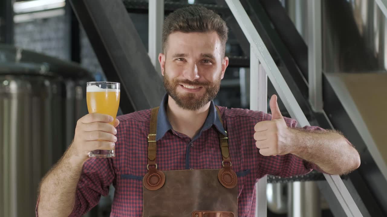 Young brewer wearing a leather apron is tasting beer at a modern brewery