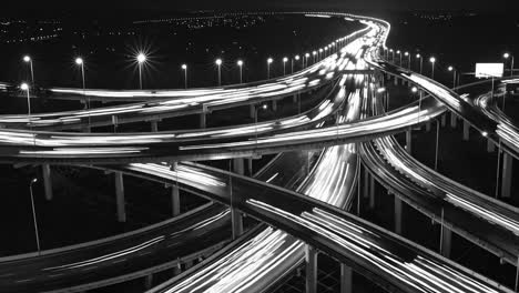 nighttime highway interchange with flowing light trails revealing intricate roadway network's dynamic motion in dramatic black and white visual sequence