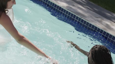 two diverse teenage female friends having fun playing with inflatables in swimming pool, slow motion