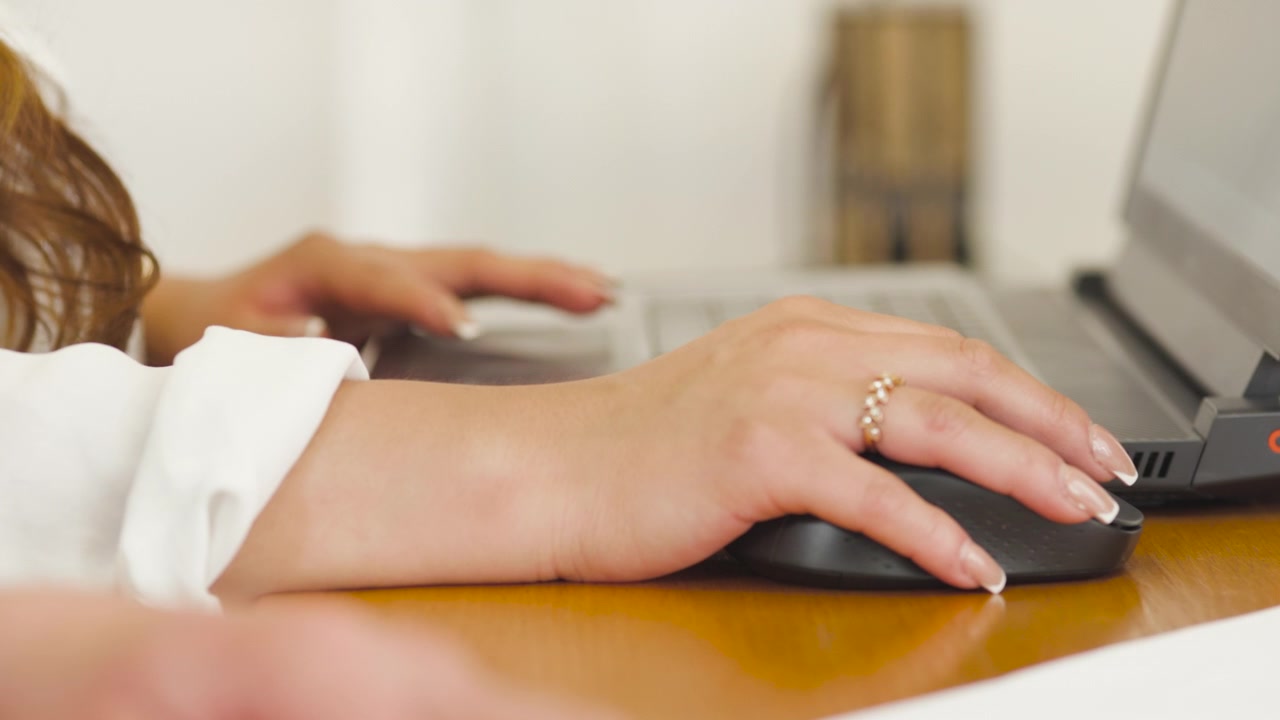 Primo piano che mostra le mani di una persona che usa un mouse e una tastiera di un laptop su una scrivania di legno