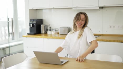 Mujer-Rubia-Hace-Videollamadas-En-Línea-En-Una-Laptop-Mientras-Camina-Por-La-Cocina-En-Pijama