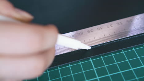 skilled tailor draws line on leather cloth with white pen