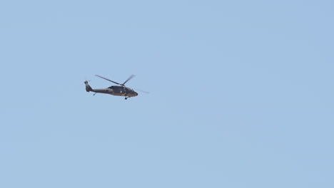 slow motion: military helicopter hovers in the cloudless blue sky from a distance