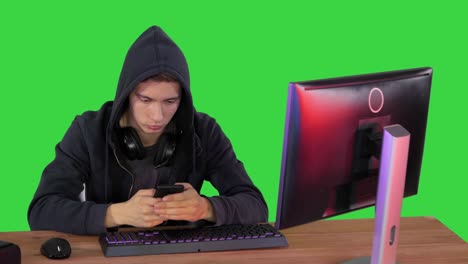 hacker encapuchado usando portátil y teléfono inteligente en una pantalla verde, clave de croma