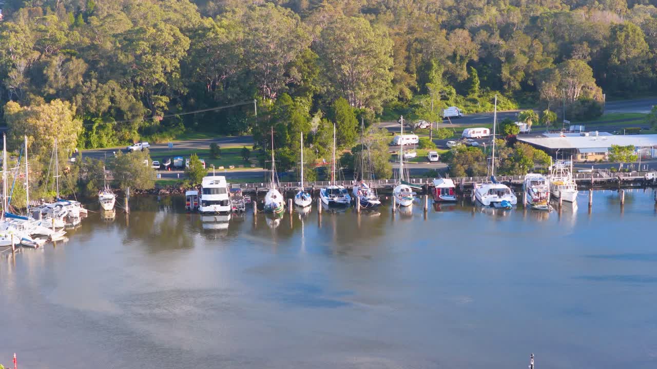 Aerial footage captures boats docked at a serene marina surrounded by lush greenery under bright daylight