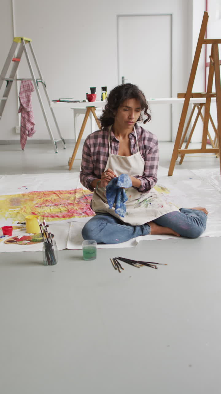 video vertical de una artista femenina biracial pintando en el suelo en el estudio